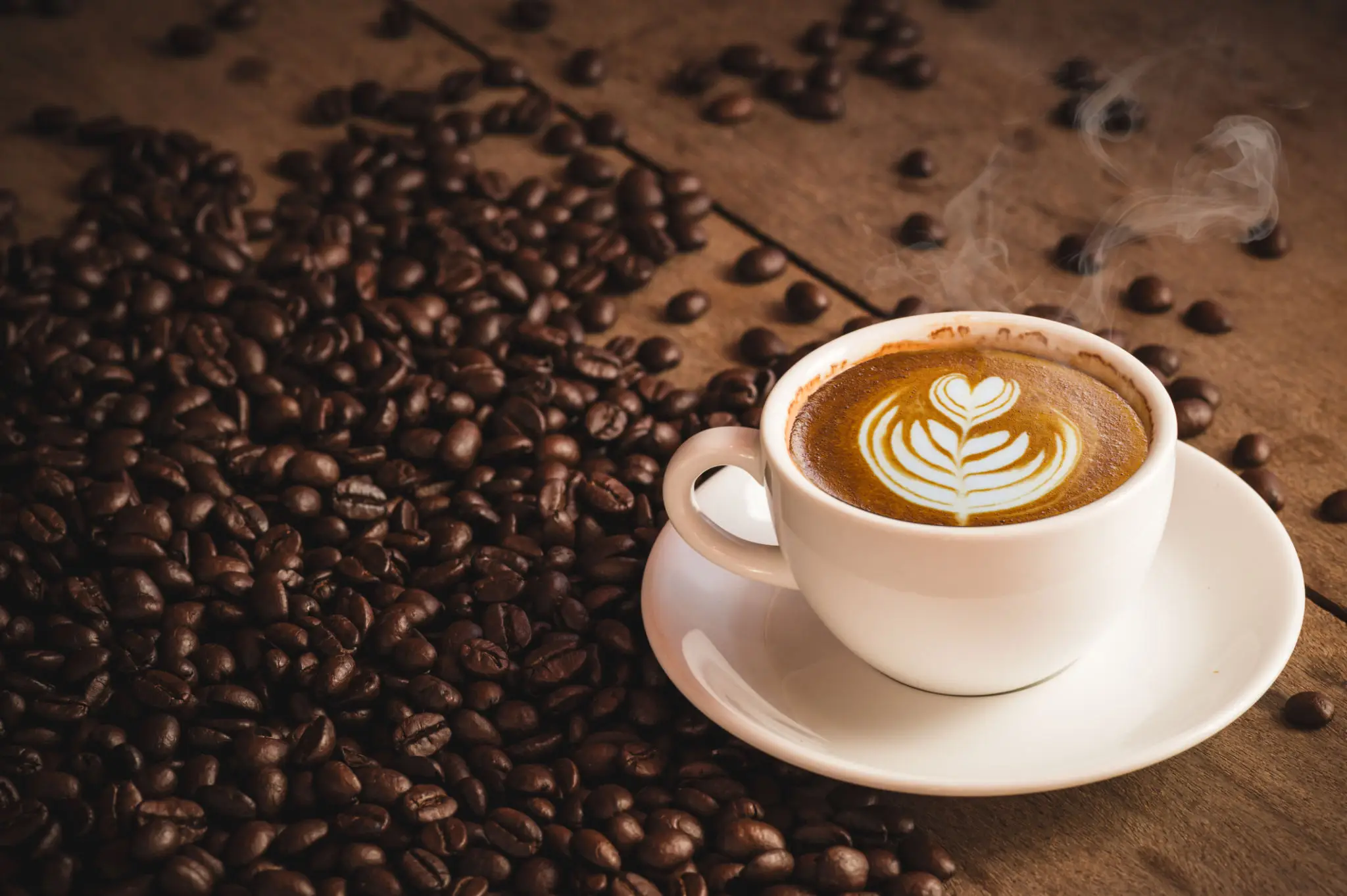 A cup of latte with latte art next to coffee beans.