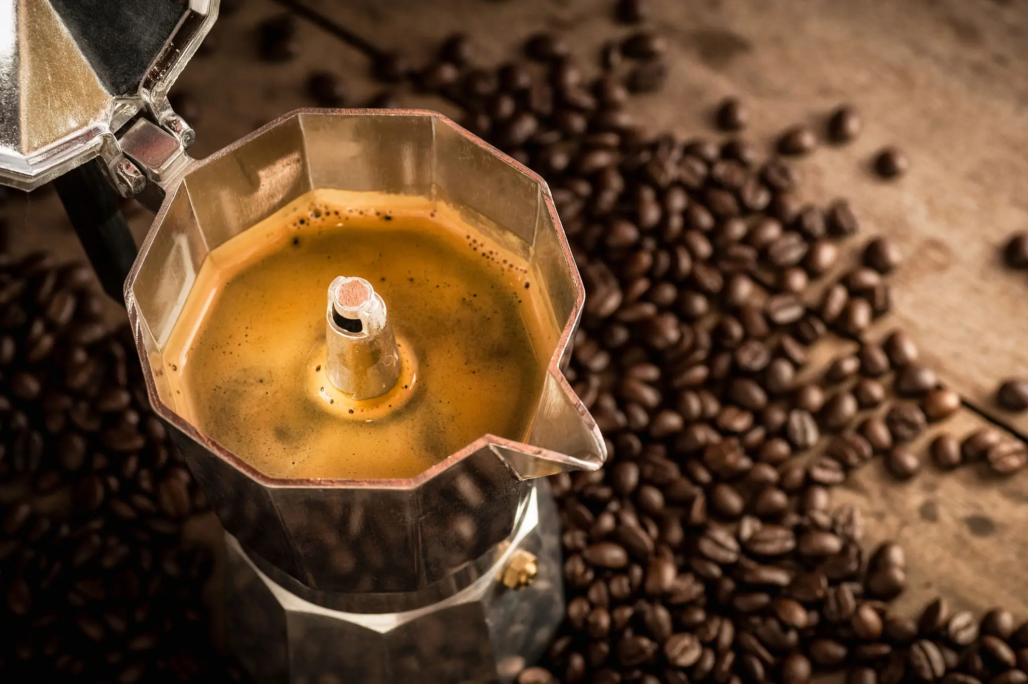 Close-up of coffee brewing in a stovetop espresso maker with scattered coffee beans.